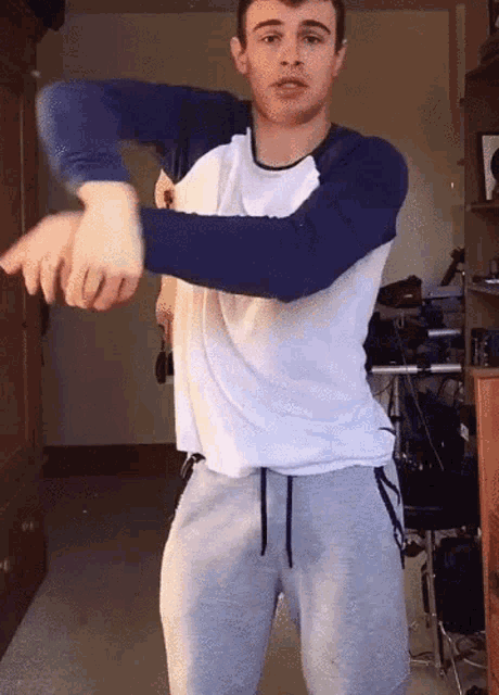 a young man in a blue and white shirt and grey sweatpants is dancing