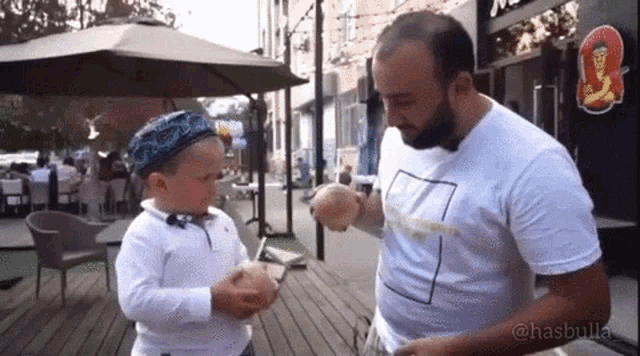 a man and a little boy are eating hamburgers on the sidewalk .