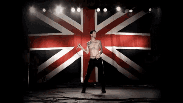 a shirtless man stands on a stage in front of an british flag