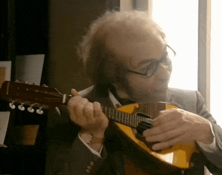 a man in a suit is playing a mandolin in front of a window .