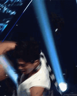 a man in a white tank top is dancing on a stage with a blue light behind him