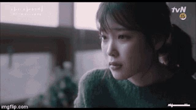 a close up of a woman 's face with her eyes closed and a green sweater on .