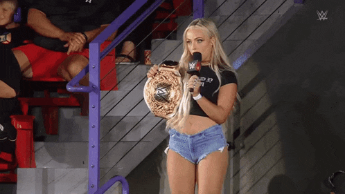 a woman is holding a wrestling championship belt and speaking into a microphone with a w logo in the background