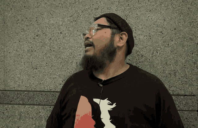 a man with a beard is wearing glasses and a black shirt with a picture of a bear on it
