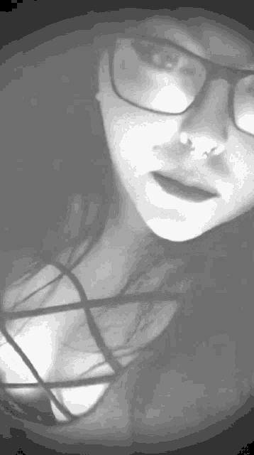 a woman wearing glasses and a nose ring looks at the camera in a black and white photo .