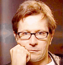 a man wearing glasses rests his chin on his hand