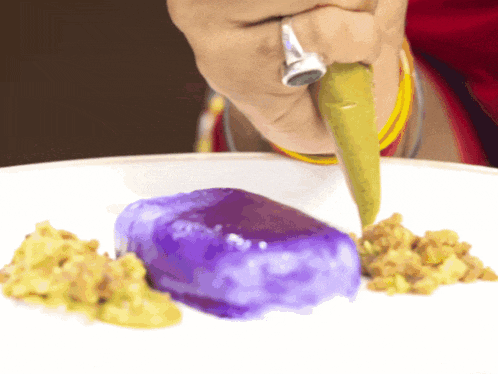 a person with a ring on their finger is icing a purple dessert