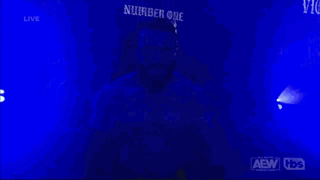 a wrestler is walking through a tunnel with a aew logo on the bottom right