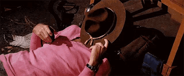 a person in a pink sweater is laying on the ground with a hat on their head .