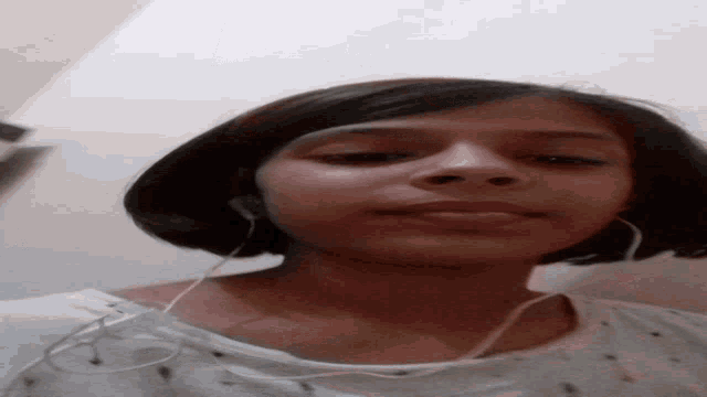 a woman wearing headphones and a white shirt looks down at the camera