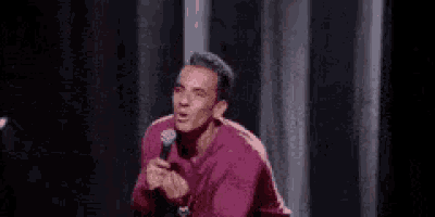 a man in a purple shirt is holding a microphone and making a funny face .