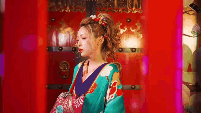 a woman in a kimono stands in front of a red door .