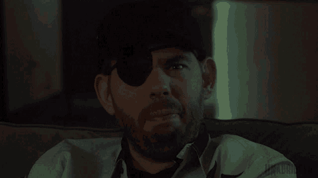 a man wearing a patch on his eye is sitting on a couch in a dark room