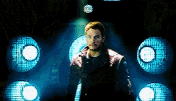 a man in a pink jacket is standing in a dark room with blue lights behind him