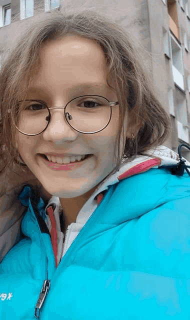 a young girl wearing glasses and a blue jacket with a zipper that says ' x9x ' on it