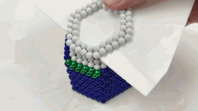 a person is holding a piece of paper with a necklace made of beads on it