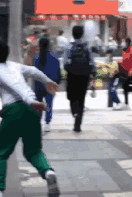 a blurry picture of people walking down a street with one wearing a white shirt that says ' a ' on it