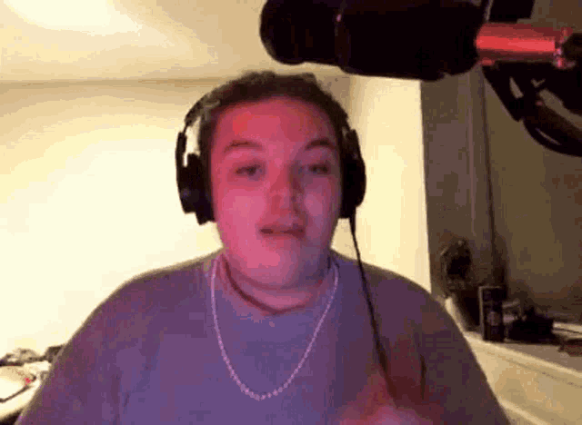 a man wearing headphones and a necklace is standing in front of a microphone .