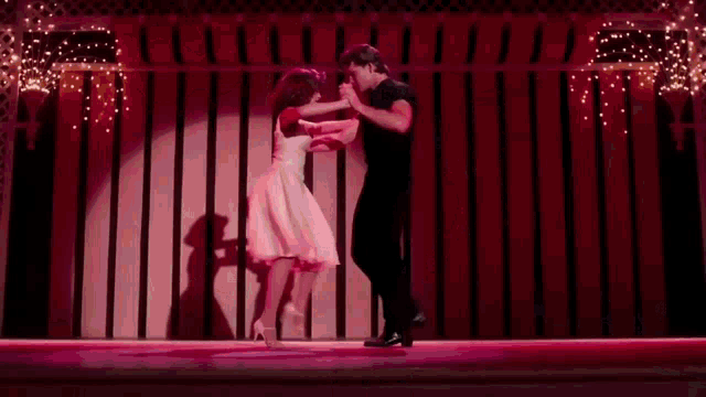 a man and a woman are dancing together in a dark room with pink lights .