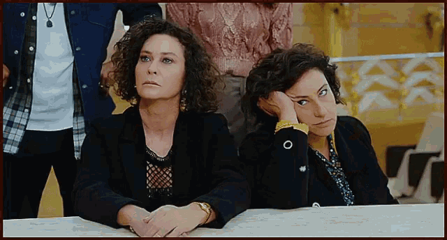two women are sitting at a table with their hands on their chins