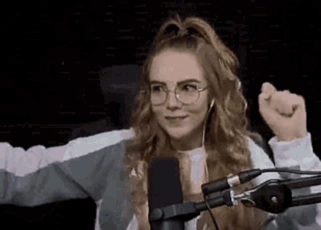 a woman wearing glasses is sitting in front of a microphone with her arms outstretched .