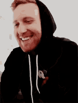 a man wearing a black hoodie is smiling while sitting on a couch .