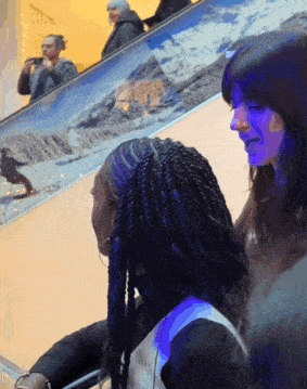 two women sitting in front of a painting of mountains