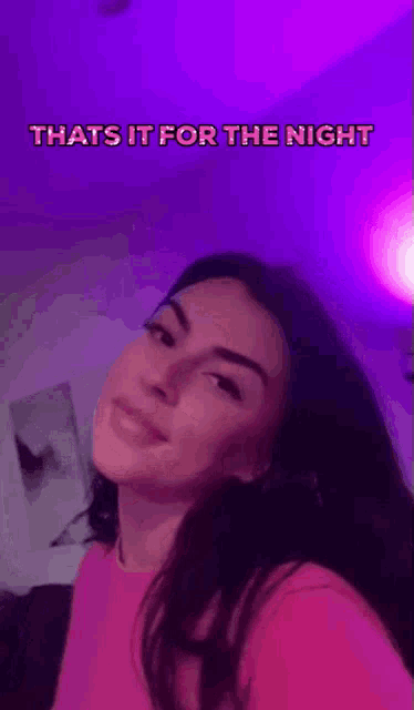 a woman in a pink shirt is smiling in front of a purple wall .