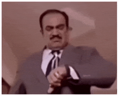 a man in a suit and tie is looking at his watch and making a funny face .