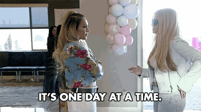 two women standing next to each other with the words it 's one day at a time above them