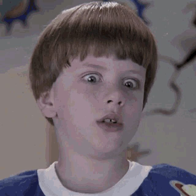 a young boy wearing a blue shirt with a planet on it is making a funny face