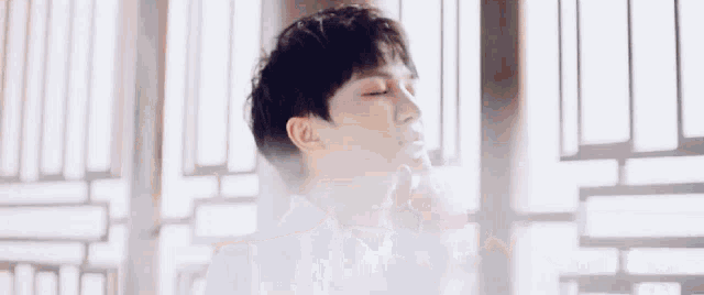 a young man is standing in front of a window with his eyes closed and smoke coming out of his mouth .
