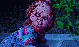 chucky doll from child 's play is looking at the camera with a purple background .