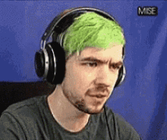 a man with green hair is wearing headphones and looking at the camera .