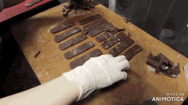 a person wearing white gloves is cutting chocolate on a cutting board that says made in animotica