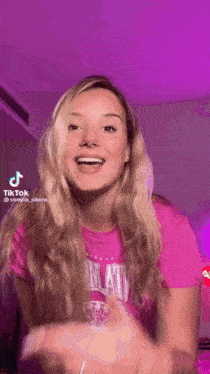 a woman in a pink shirt is making a funny face while standing in front of a purple background .