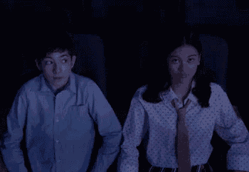a boy and a girl are sitting next to each other in a dark room watching a movie .