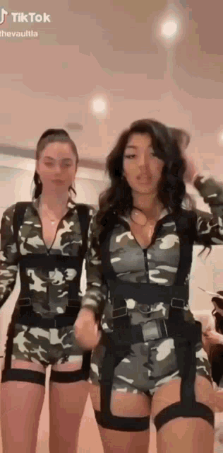 two women in camouflage outfits are standing next to each other and dancing .