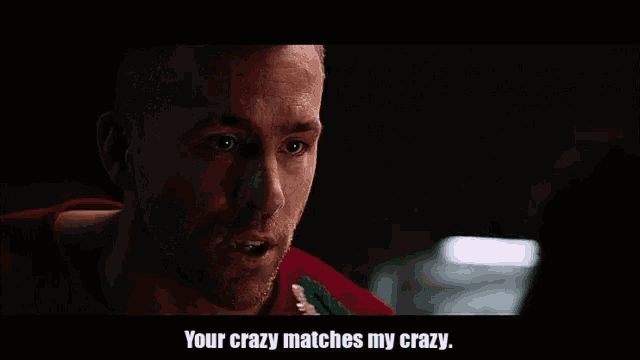 a man in a red sweater is talking to another man in a dark room and says `` your crazy matches my crazy '' .