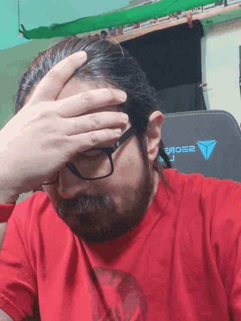 a man wearing glasses and a red shirt has his hand on his face