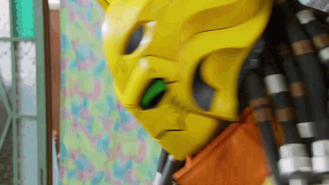 a yellow predator mask with a green eye is hanging on a wall