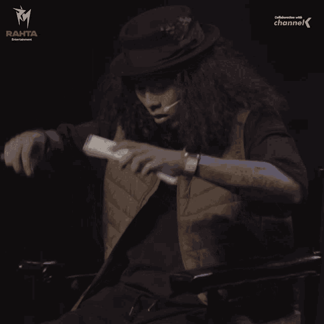 a man with long curly hair is sitting in a chair in front of a rahta logo