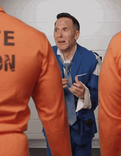 a man in a blue suit and tie is standing next to a man in an orange uniform with the letter e on the back
