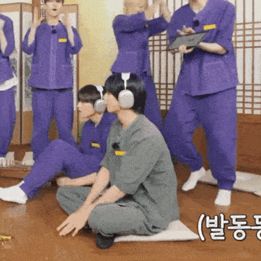a man wearing headphones sits on the floor in front of a group of people in purple pants