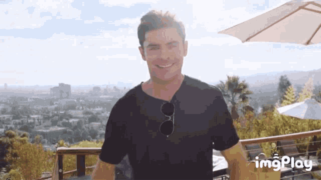 a man wearing sunglasses and a black shirt is smiling in front of a view of a city