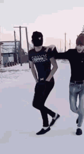 two men are dancing in the snow and one of them is wearing a black hat .