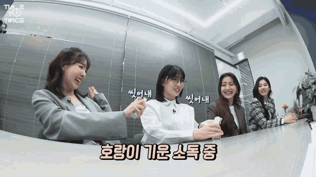 a group of women sitting at a table with a tv twice logo on the wall behind them