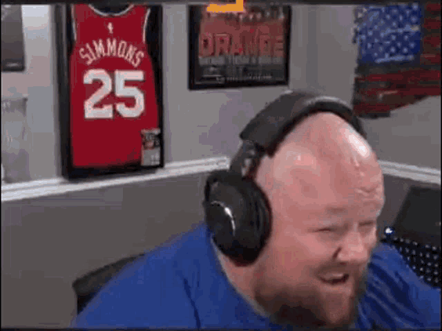 a bald man with a beard is wearing headphones and smiling in front of a basketball jersey .