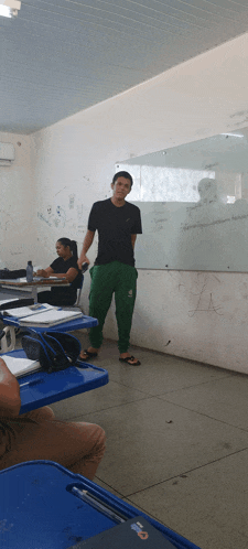 a man in a black shirt and green pants stands in front of a white board that says " a " on it