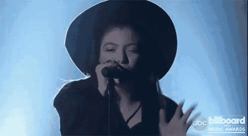 a woman in a black hat is singing into a microphone at the billboard music awards .